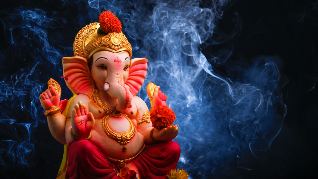 A vibrant Ganesh idol adorned with marigold flowers, set against a dark background with swirling blue smoke.